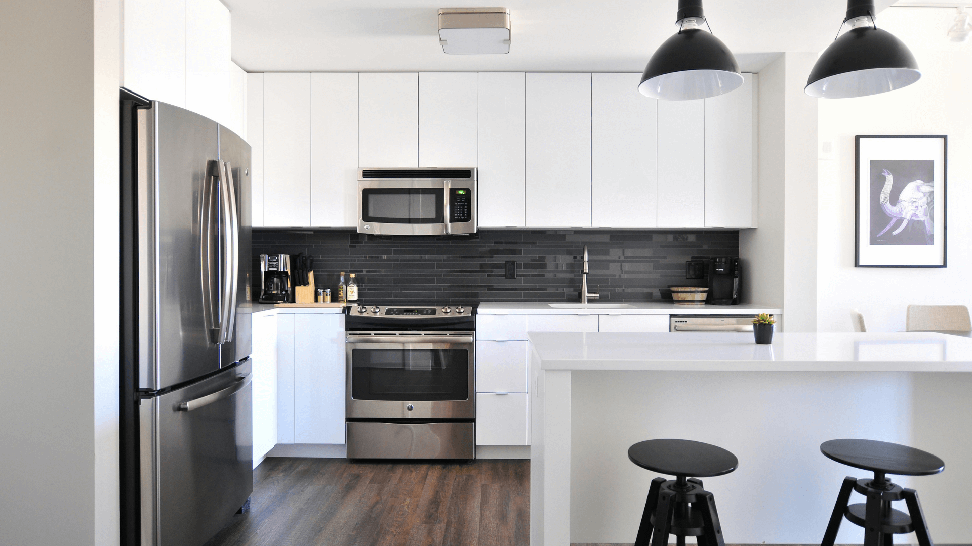 A stylish modern kitchen with white cabinets, marble countertops, and stainless steel appliances.